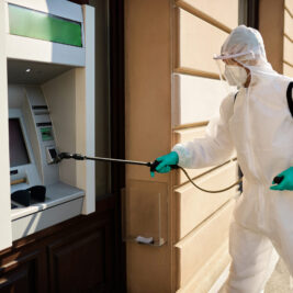 Disinfectant worker in protective suit cleaning ATM in the city due to COVID-19 epidemic.